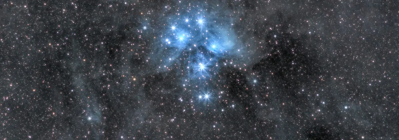 Dark night sky filled with starts and a blue galaxy at center