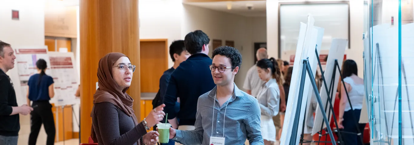 "Man and woman talk in the midst of conference research posters"