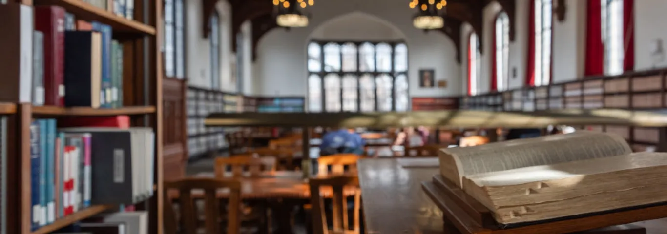 Photograph of a library with an open volume in the foreground and arched windows behind