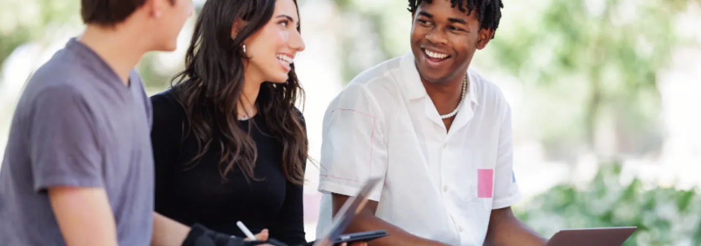 "Three students in conversation, sitting outdoors"