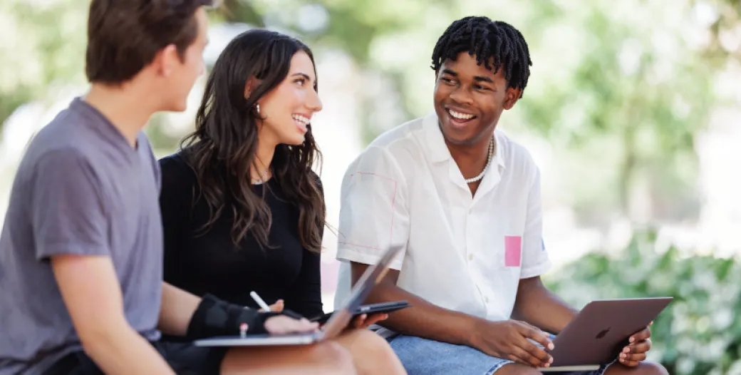 "Three students in conversation, sitting outdoors"