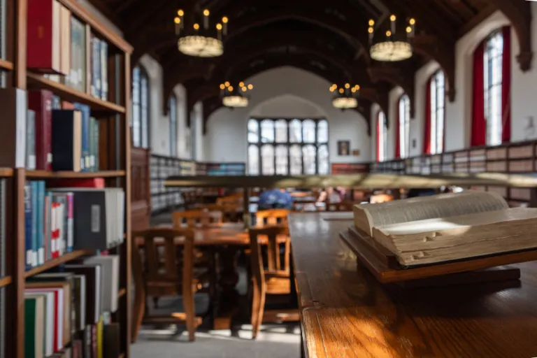 Photograph of a library with an open volume in the foreground and arched windows behind